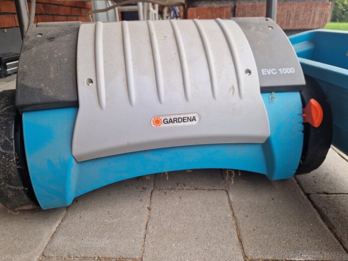 Blå och grå Gardena EVC 1000 vertikalskärare på en stenlagd uteplats.