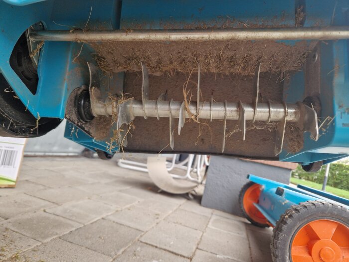 Vertikalskärare med gräsrester, fotograferad på en stenlagd yta.