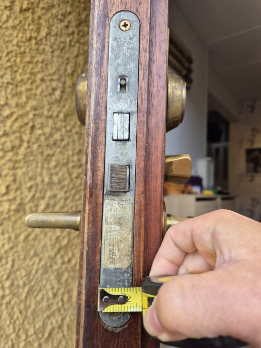 Mätning av dörrlås och handtag med måttband på en brun träyta.