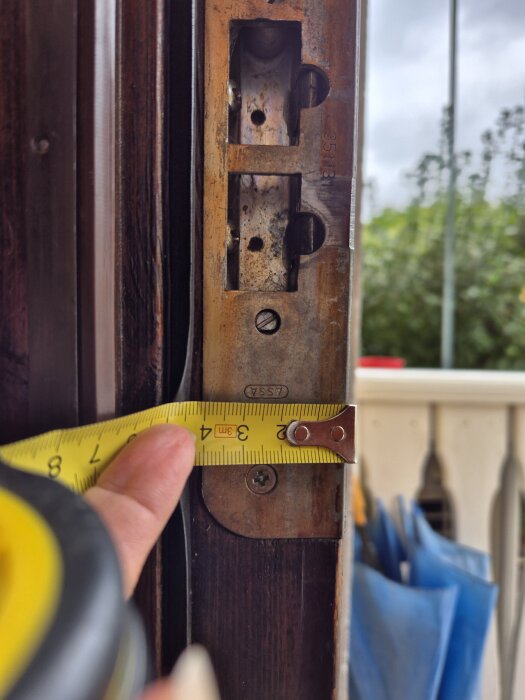 Mäta avståndet på en dörrkarm med ett måttband vid låsbeslag.
