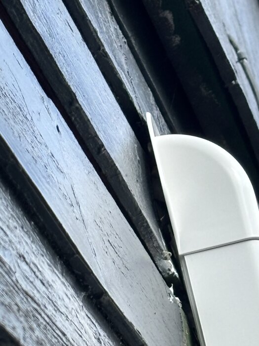 Vit 90-graderskanal på en vägg, där en springa syns, och slangar kommer ut genom väggen bakom kanalen.