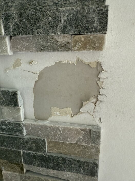 Vägg med delvis borttagen sten och synlig tapet under, redo för renovering med kakel på nederdelen och färg på övre delen.