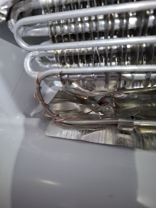 Närbild av frysens insida med synliga metallrör och kopparkabel.