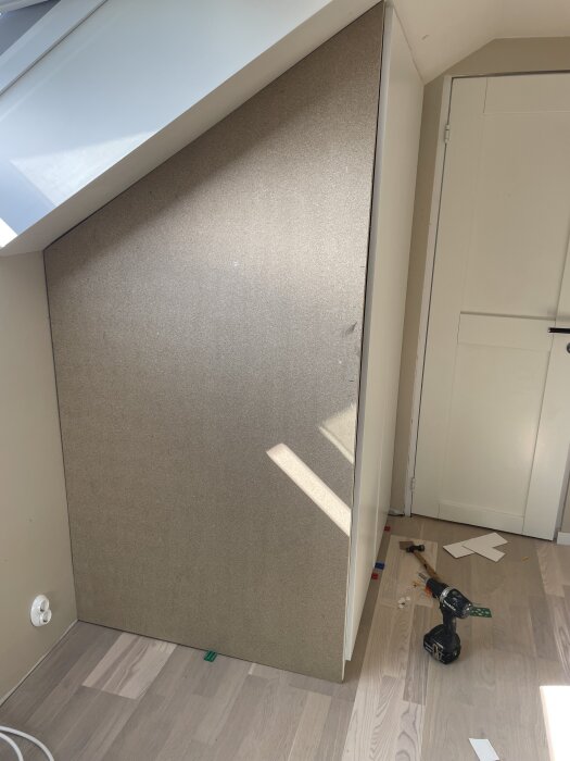 Massonitpanel lutad mot en garderob i ett rum, omgiven av verktyg som en skruvdragare och hammare på golvet.