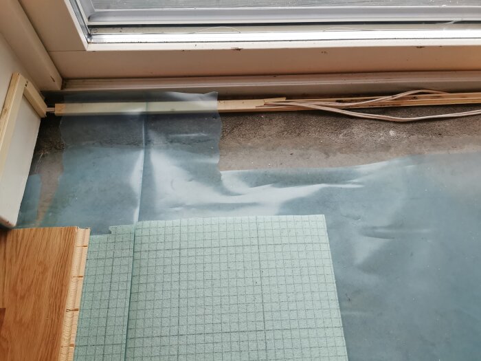Golvinläggning nära altandörr, visar underlag och träplatta med isoleringsmaterial för att undvika fuktproblem.
