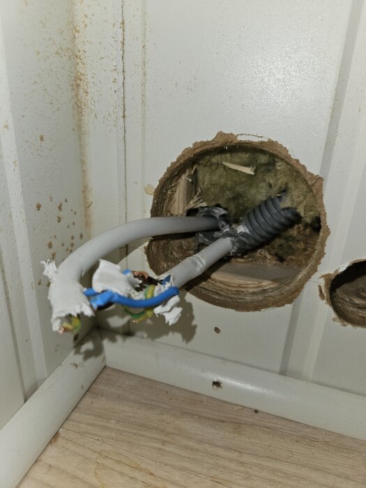 Skadad elledning i borrat ventilationshål i en vägg, omgiven av isoleringsmaterial och trä.