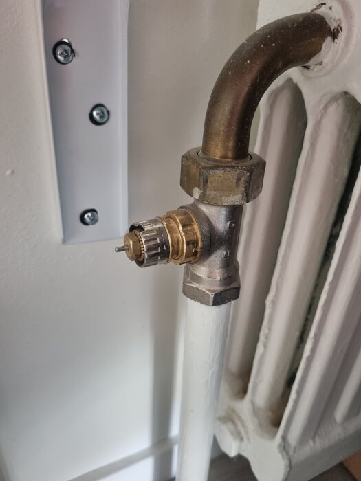 Äldre element med vinklad koppling och anslutning för termostat, fotat i närbild.