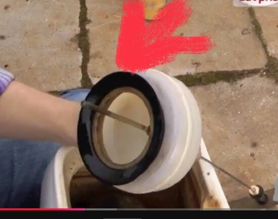 Hand håller en trasig del av gammal IFÖ-toalett, markerad med röd pil, för reparation eller reservdelsbyte.