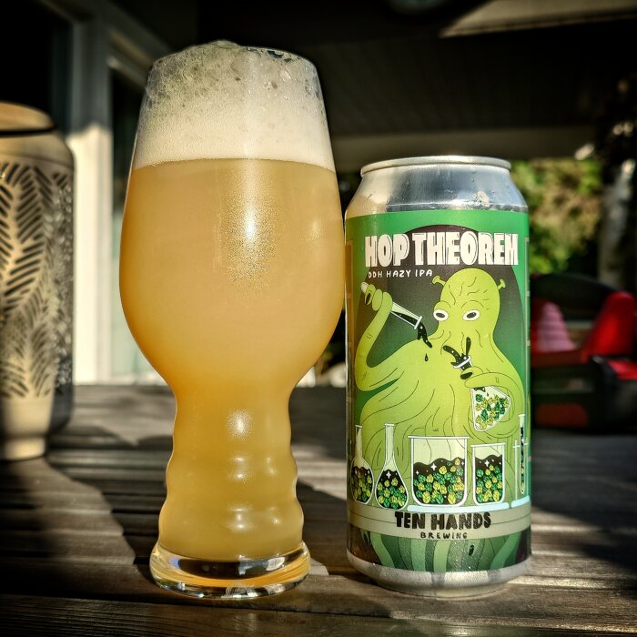 Bryggd öl i glas bredvid en burk med etiketten "Hop Theorem" från Ten Hands Brewing på ett bord utomhus.