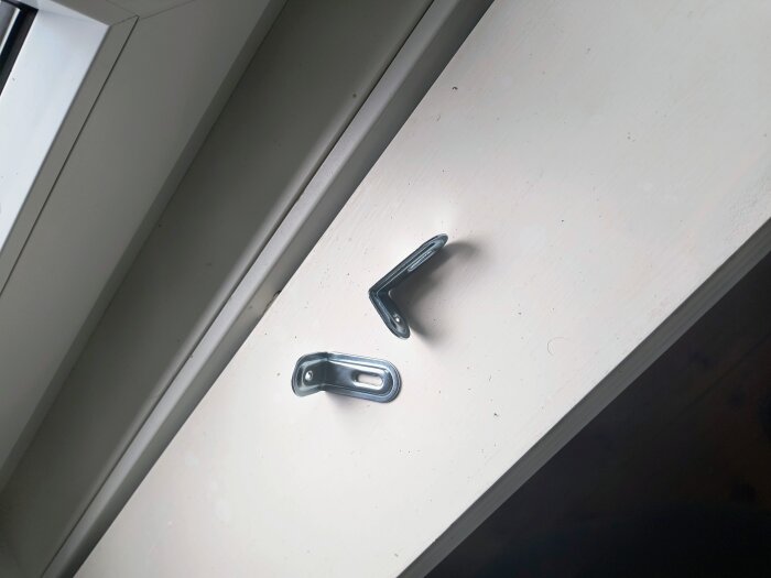 Två metallvinklar monterade på en vit träram, en del av konstruktionen för hemmagjorda myggfönster.