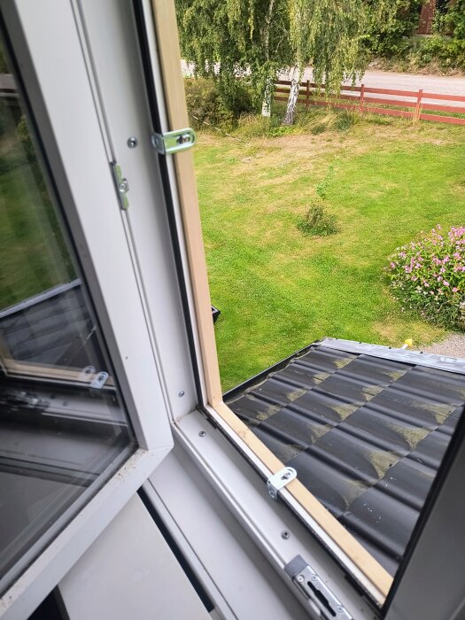 Hembyggt myggfönster monterat i ett fönster med utsikt över en grönskande trädgård och tak i plåt.