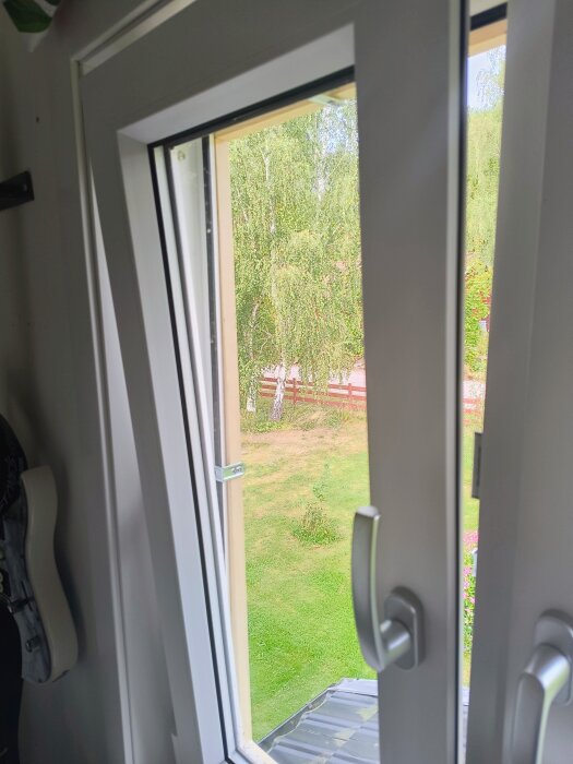 Öppet fönster i vädringsläge med utsikt över en somrig trädgård, del av projekt för att bygga egna myggfönster med fururamar och myggnät.