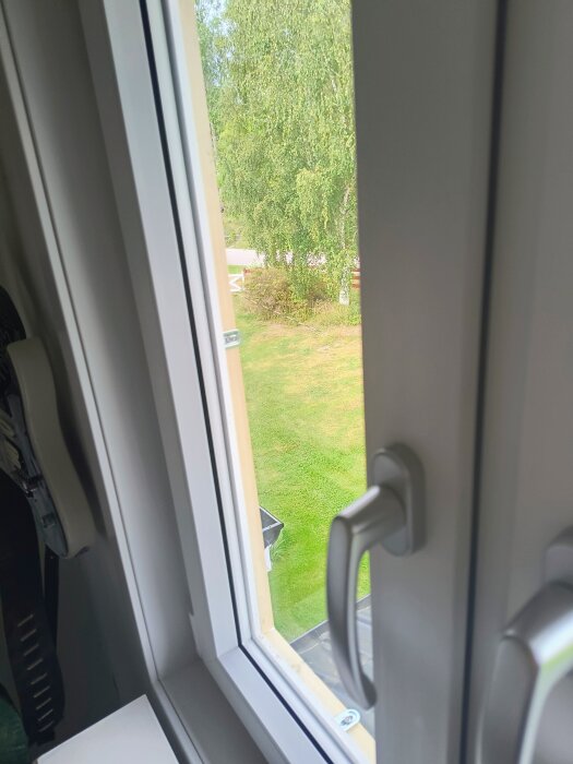 Öppet fönster med utsikt över trädgård, visar handtag och träram för hemmagjort myggfönster enligt beskrivning i inlägget.