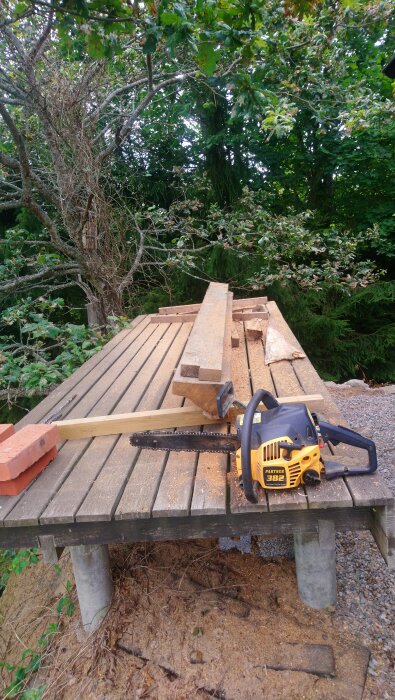 Träbit och motorsåg på träbord utomhus, omgiven av gröna träd.