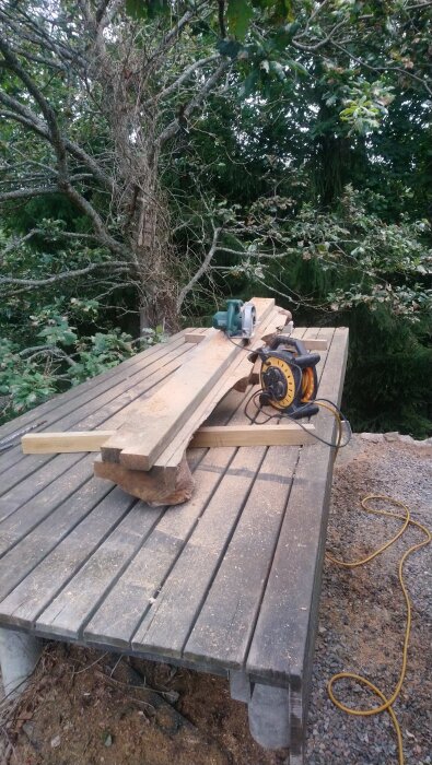 Brädor på ett utomhusbord med en cirkelsåg och elsladd, omgiven av träd. Denna ek planka har funnits sedan två träd fälldes för 10 år sedan.