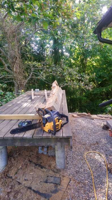 Motorsåg och ekstock på trädäck med skog i bakgrunden.