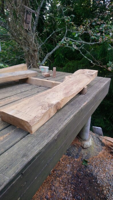 Hyvlade och sågade träplankor på en träbänk utomhus, omgiven av träd.