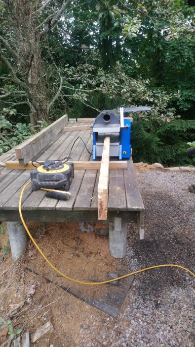 Hyvelbänk utomhus med en planka i en planhyvel och en förlängningssladd på bordet.