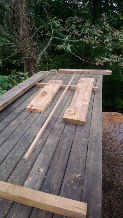 Hyvlade och sågade träbitar ligger utspridda på ett träbord i en skogsmiljö.