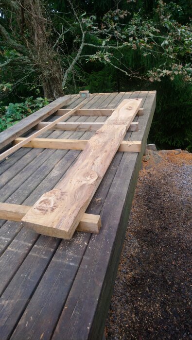 Grovhyvlad plank på en arbetsbänk utomhus, omgiven av natur och spån på marken.