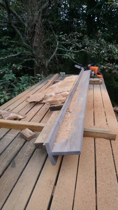 Brädor och sågspån på ett bord utomhus, med en motorsåg vid sidan.