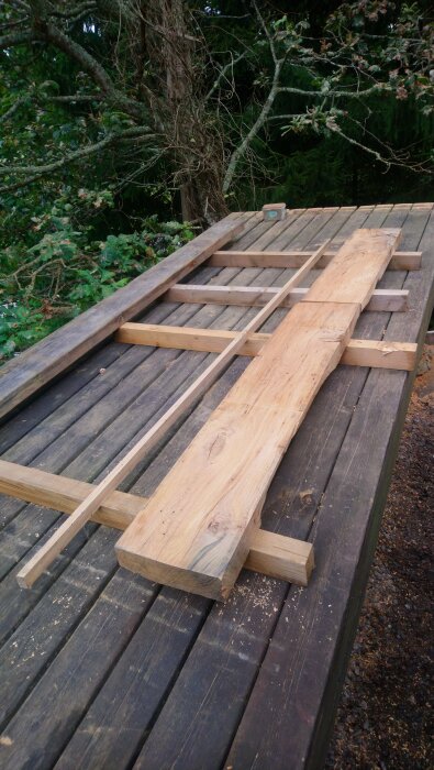 Hyvlade och sågade träplankor ligger på ett bord utomhus, omgivna av träd.