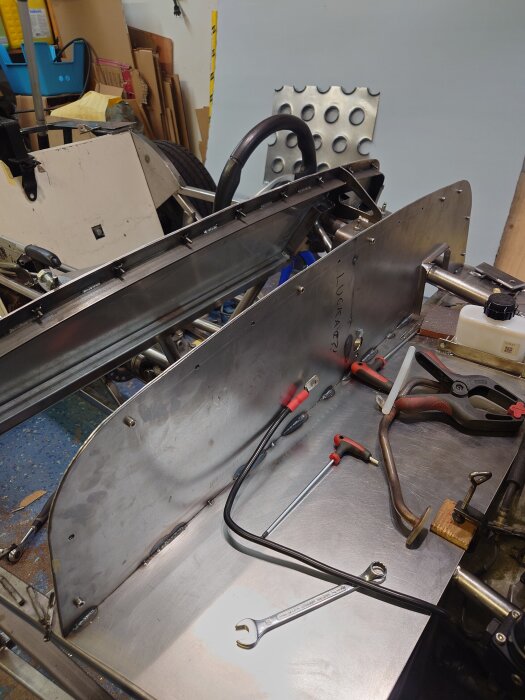 Arbetsbänk med verktyg och metallplåt. Verktyg inklusive skruvmejslar och skiftnyckel ligger på plåt vid konstruktion.