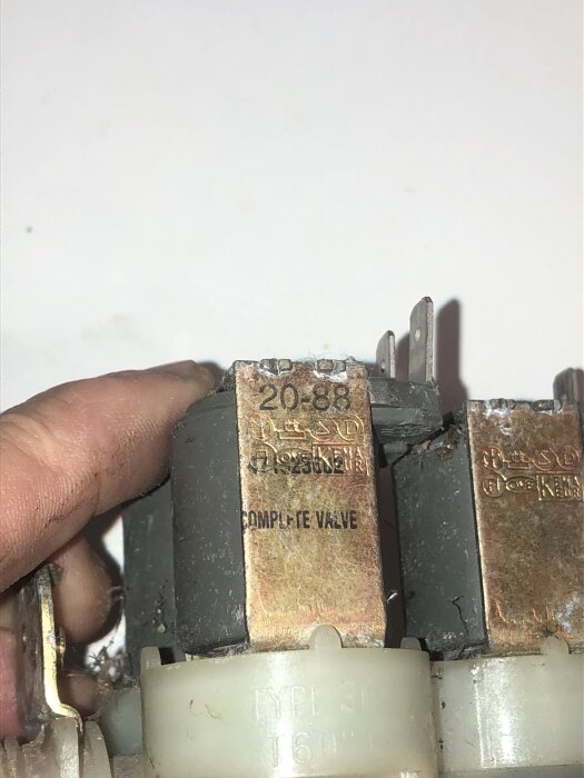 En närbild av en hand som håller en rostig ventil märkt "20-88" med texten "COMPLETE VALVE".