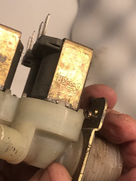 Närbild på en person som håller en guldfärgad och vit komponent, möjligen en ventil, med tekniska märkningar.