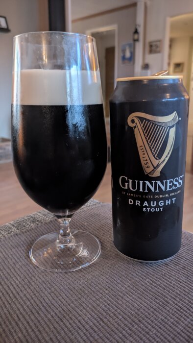Ett glas Guinness med en burk bredvid, ståendes på ett bord i ett hemtrevligt rum.