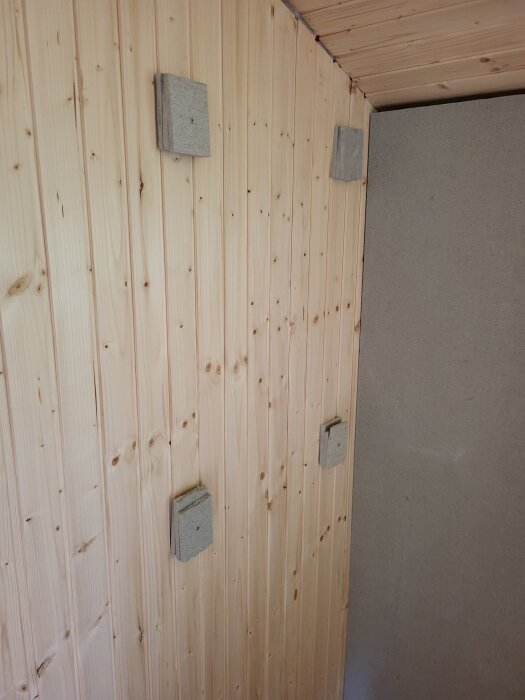 Vägg med träpanel och små rektangulära betongplattor monterade på ytan.