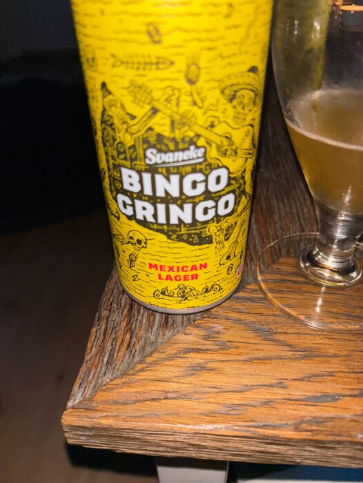 Svaneke Bingo Gringo Mexican Lager-burk på ett träbord bredvid ett halvtomt glas.