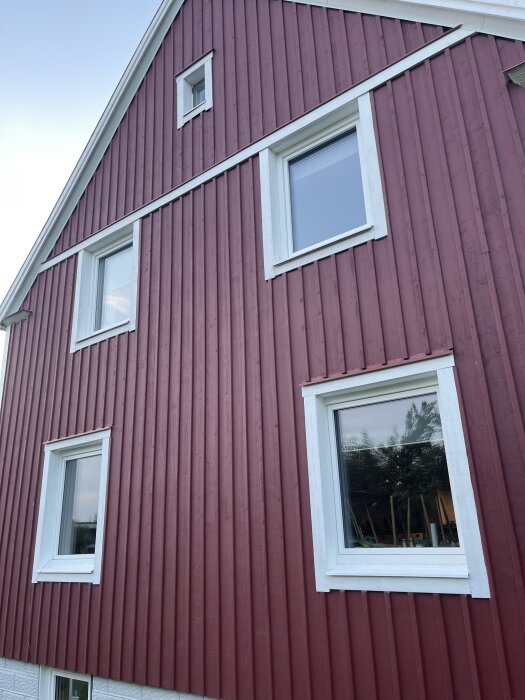 Röd träfasad med tre vita PVC-fönster, där två är stora och ett är litet.