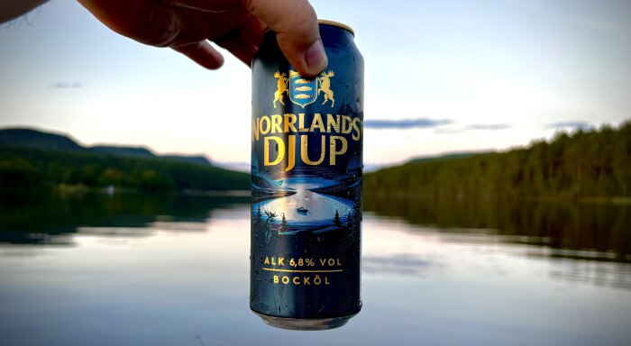 Dryckesburk med "Norrlands Djup" hålls i handen framför en sjö och skog i skymning, texten lyder: "Tror fan jag hittat stället. 😅