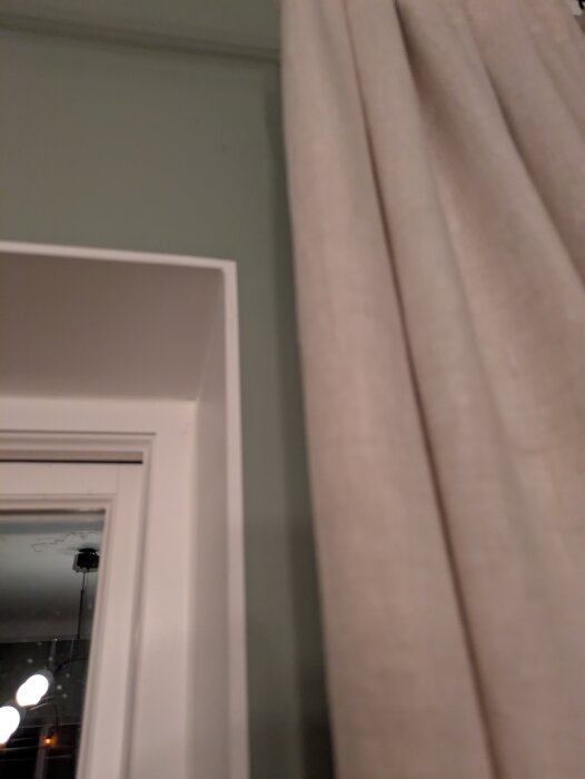 Vägg nära fönster med grön färg och gardin, visar snobbkant mot taket och vitt fönster.