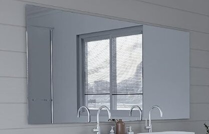 Väggmonterad spegel i badrum, speglar fönster med persienner och kranar nedanför, ger sken av vara svävande med skugga mellan spegeln och väggen.