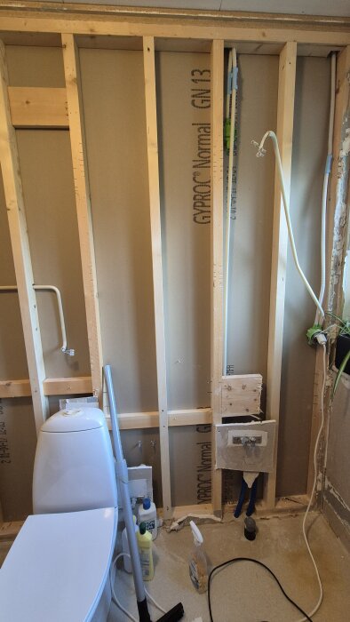 Renovering av badrum med avskalade väggar med trästomme och gipsskiva, synliga rör, en toalettstol, städutrustning och rengöringsmedel.