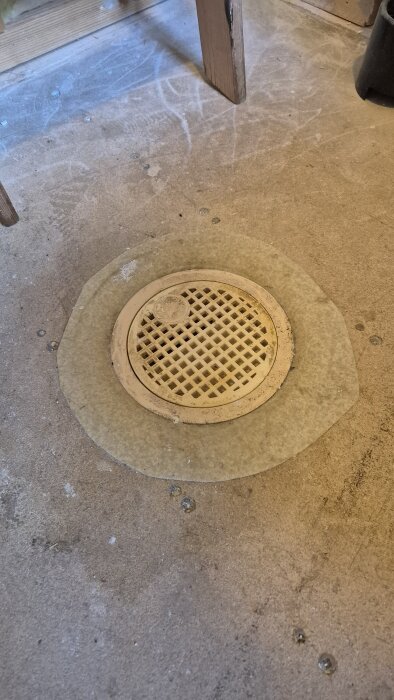 Golvbrunn i badrum med skruvlock på ett golv av spånskiva, omgiven av märkning av vattenflöde.