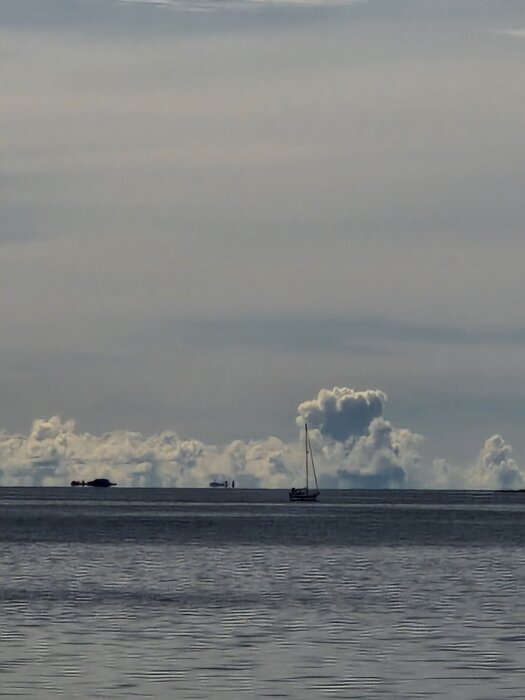 Segelbåt på havet med moln i horisonten under en molnig himmel.