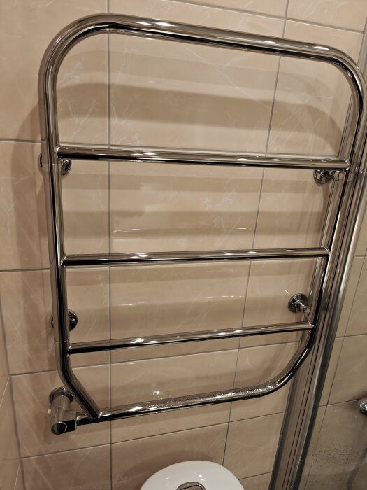 Kromad handdukstork monterad på en kaklad vägg, med flera horisontella rör och ett vred längst ner.