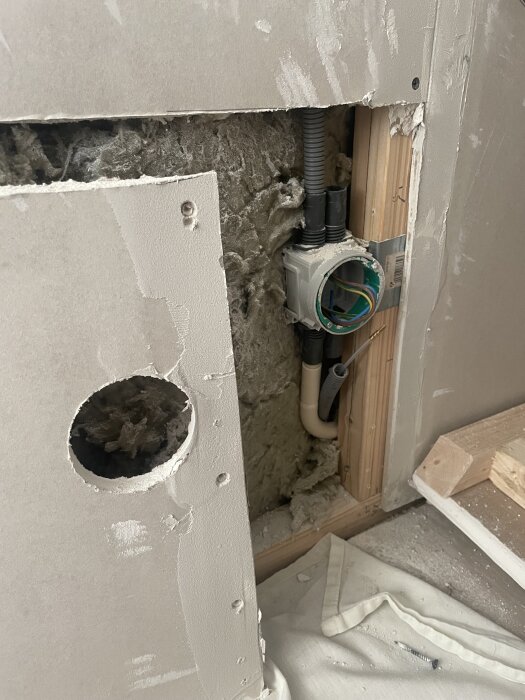 Vägg med synlig isolering och installationsbox monterad, omgärdad av öppnat gips.