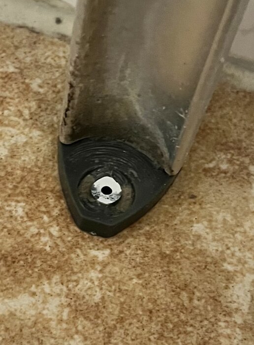 Brytpunkt för duschdörr som visar en trasig aluminiumpigg i golvet, vilket orsakade duschdörrens fall.