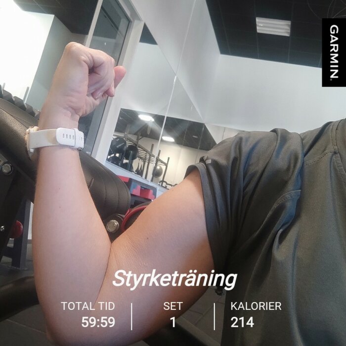En person böjer armen och spänner sin biceps i ett gym. En vit klocka syns på handleden. Texten "Styrketräning" visas med träningsstatistik.