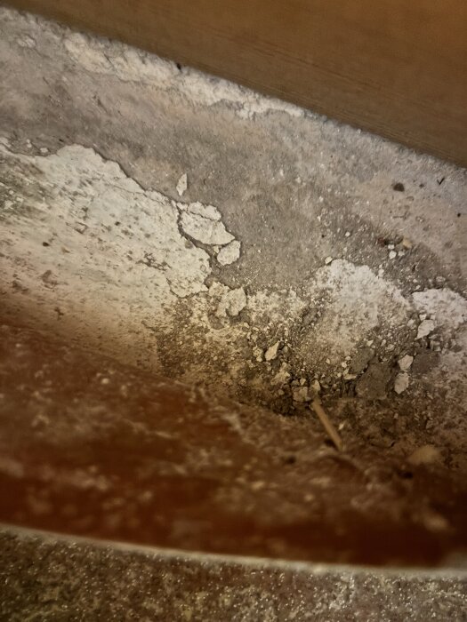 Golv med sprucket, vitt material som kan vara asbest under en gammal plastmatta.