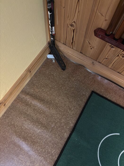 Brun plastmatta med en innebandyklubba lutad mot väggen, grönt golvunderlag syns delvis. Potentiell asbestfråga diskuterad i text.