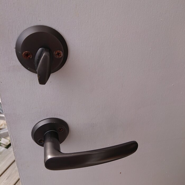 Svart dörrhandtag och lås på vit dörr, sett från insidan.