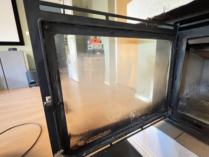 Öppen kaminlucka med synlig tätning för glas och lucka, omgiven av en vardagsrumsmiljö.