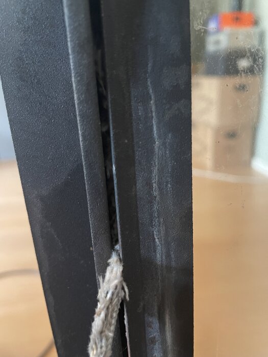 Närbild på en kaminluckas tätningslist med dubbelfunktion för glas och lucka, visar slitet material i en hemmiljö.