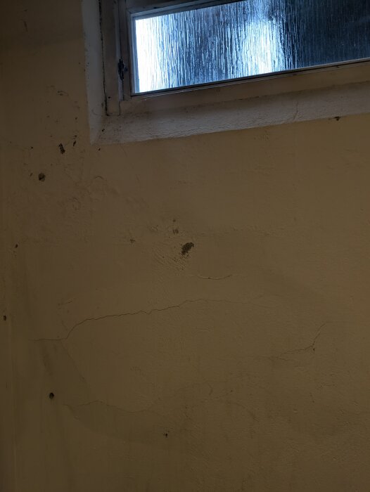 Källarvägg med sprickor och missfärgningar under ett smått fönster, del av en diskussion om renovering av badrum i ett hus från 1973.