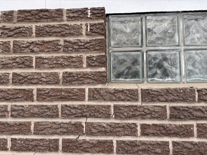 Sprickor i en brun tegelvägg bredvid glasblocksfönster.